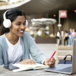 Smiling Indian woman using laptop studying, taking notes, exam preparation, online education
