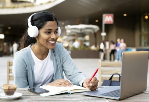 Smiling Indian woman using laptop studying, taking notes, exam preparation, online education