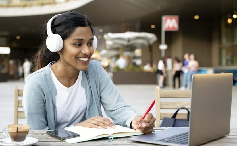 Smiling Indian woman using laptop studying, taking notes, exam preparation, online education
