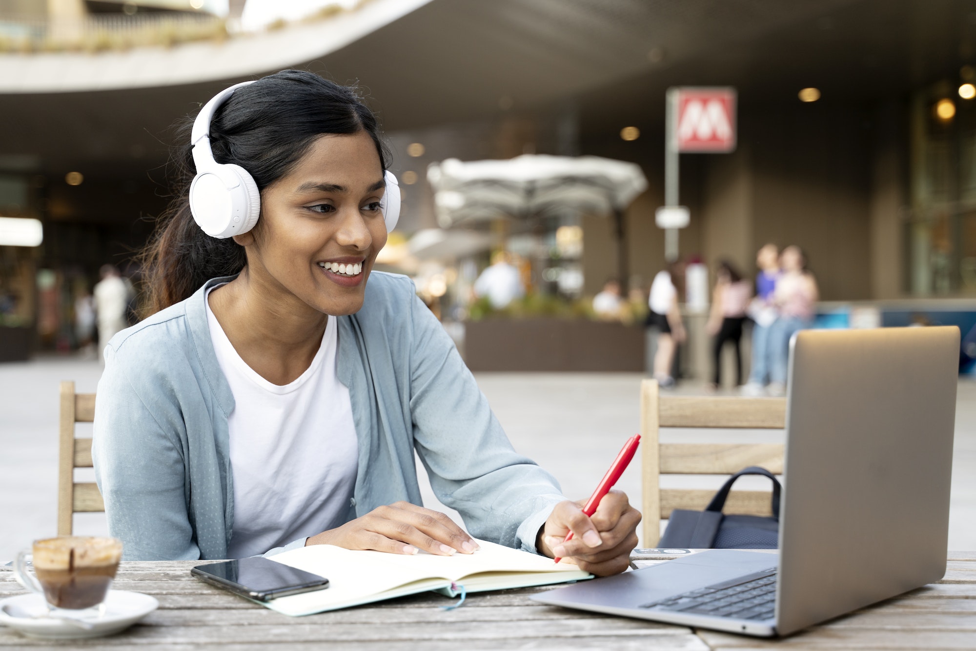 Smiling Indian woman using laptop studying, taking notes, exam preparation, online education